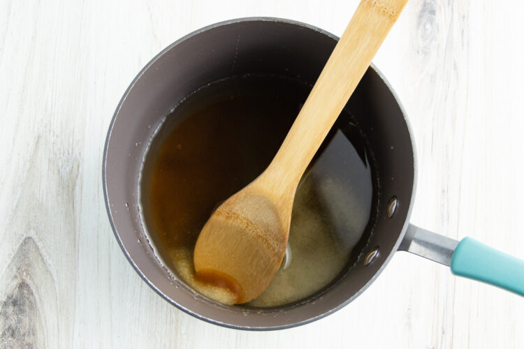 Overhead view of salt and brown sugar dissolved into a saucepan of boiling water, with a wooden spoon resting against the side of the pan.