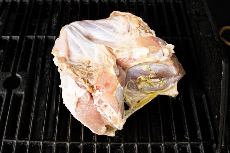 Brined and buttered turkey breast resting directly on a gas grill grate over indirect heat.