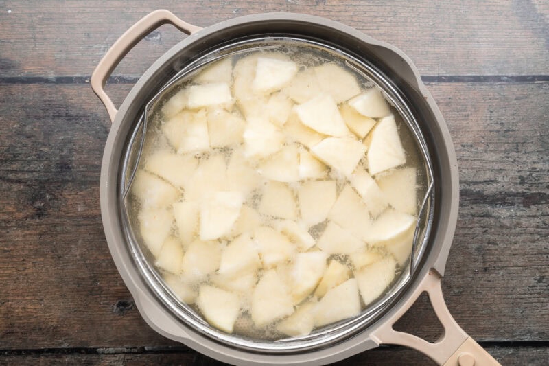 Overhead view of salted potato cubes in a large pot of water to blanch potatoes.