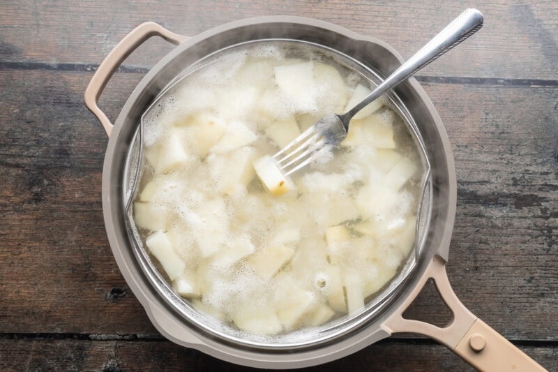 Overhead view of cubed potatoes in a large pot with simmering water.