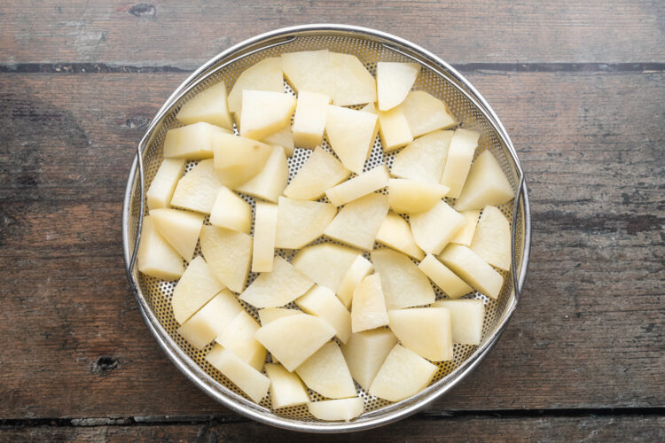 Overhead view of a bowl of cubed, blanched potatoes on a wooden tabletop.