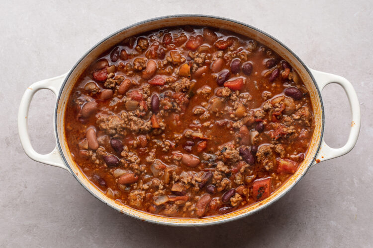 Overhead view of Mexican chili in oval chili pot on white table.