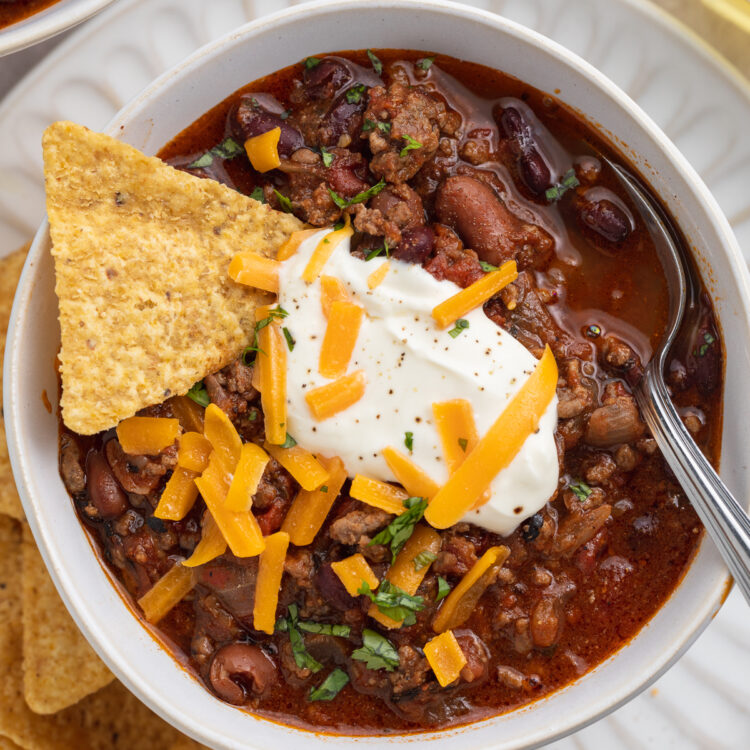 Overhead, close-up view of a bowl of Mexican chili on a white plate with tortilla chips.