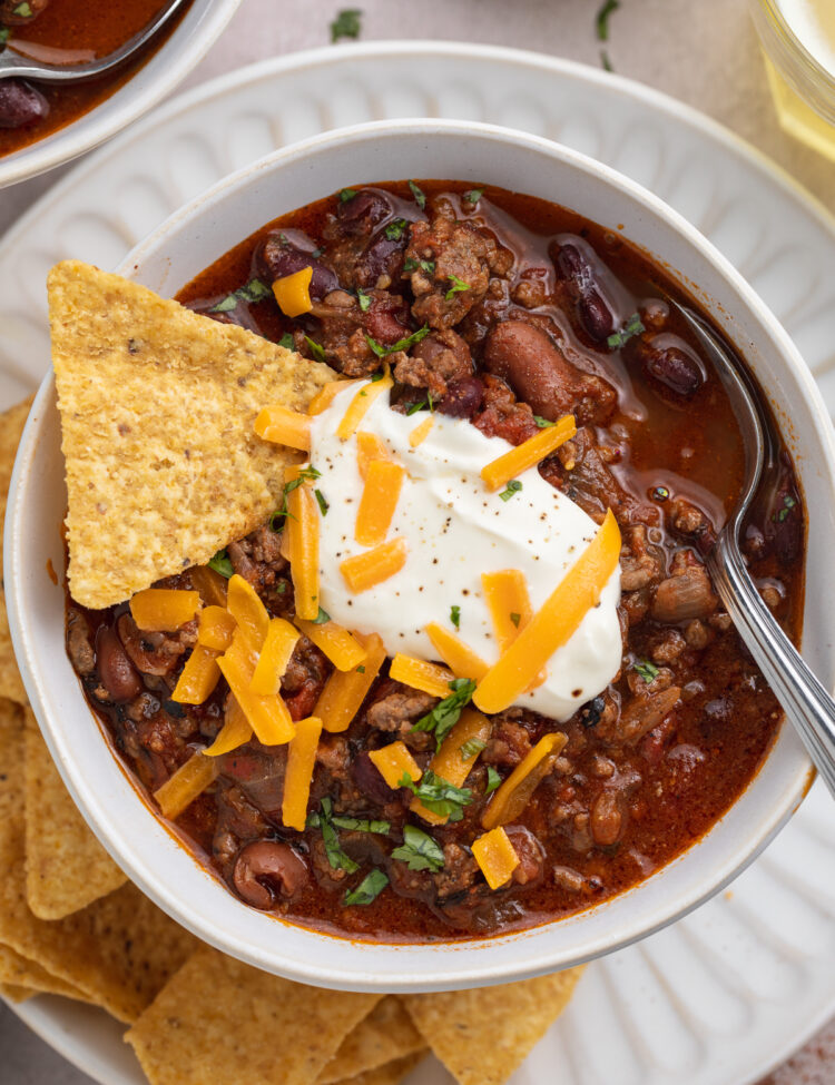 Overhead, close-up view of a bowl of Mexican chili on a white plate with tortilla chips.