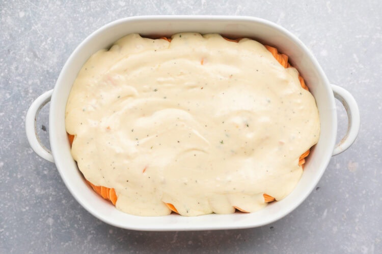 Overhead view of thinly sliced sweet potatoes covered with a creamy herb sauce in a large oval casserole dish.