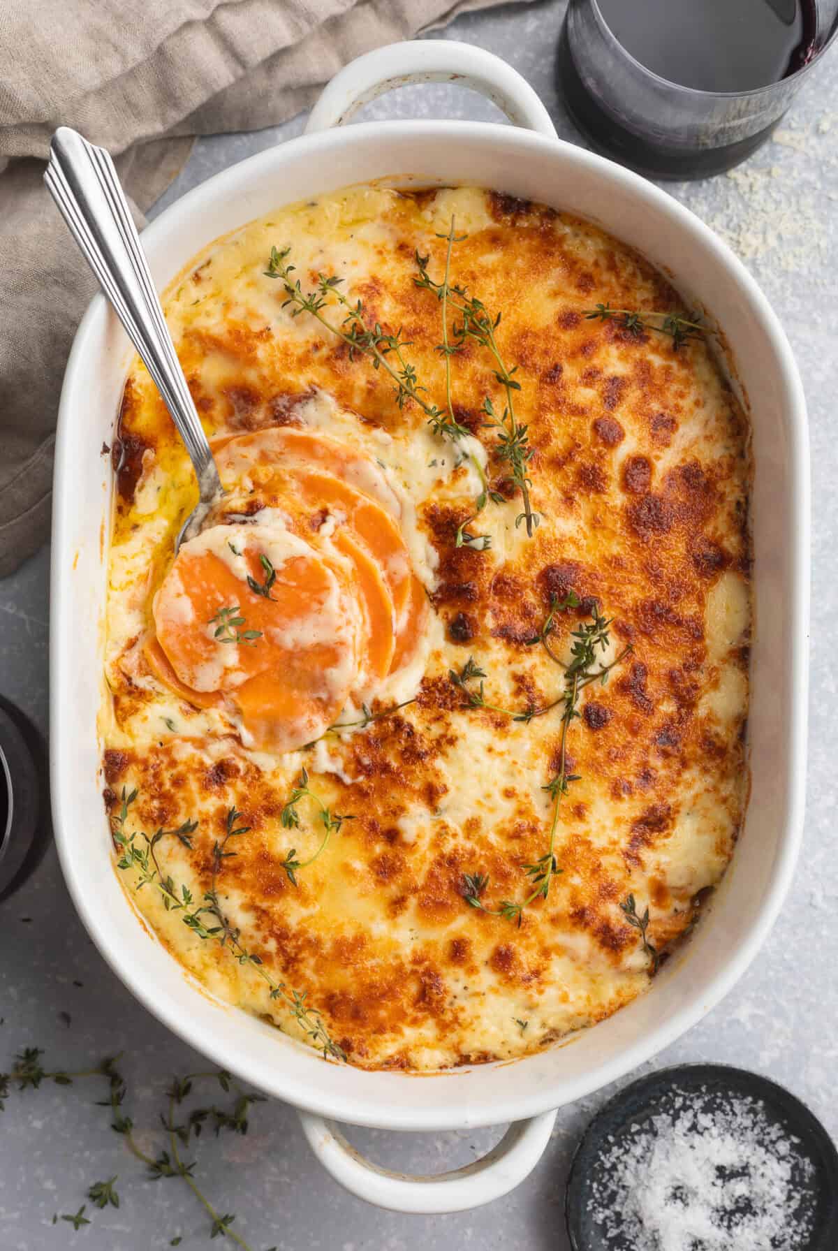 Overhead view of a large, oval casserole dish containing melty, cheesy, browned scalloped sweet potaotes.