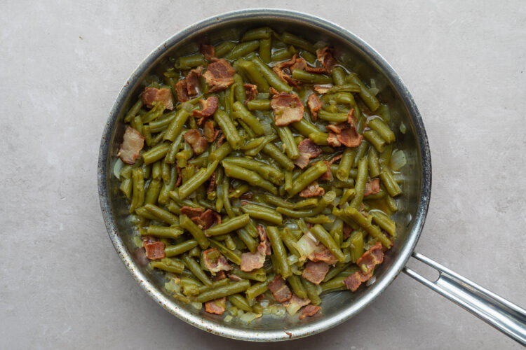 Overhead view of Texas Roadhouse green beans in a large silver skillet on a neutral countertop.