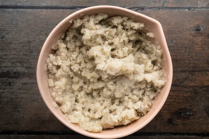 Overhead view of large beige mixing bowl holding roughly mashed potatoes.