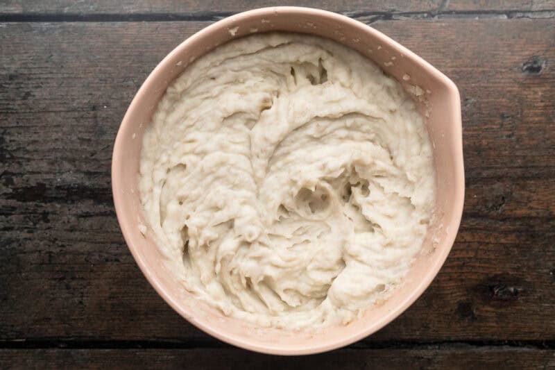 Overhead view of roughly mashed potatoes mixed with hot milk until mixture is creamy and smooth.