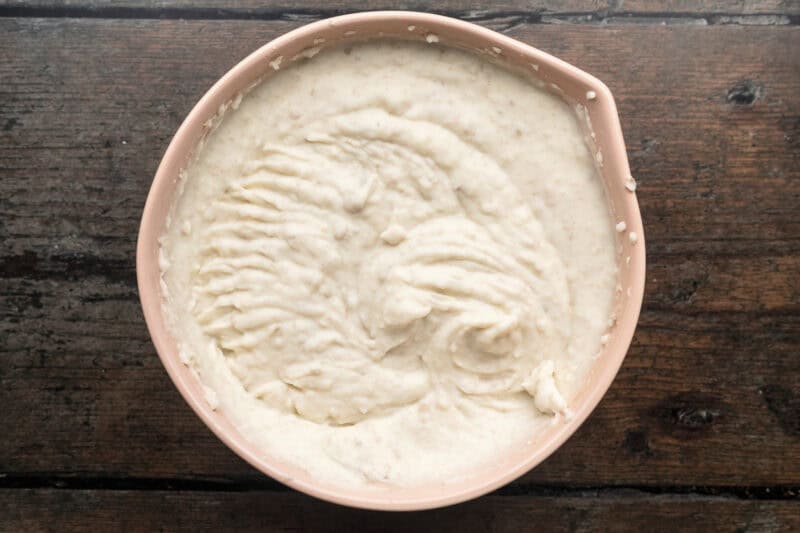 Overhead view of creamy whipped potatoes with milk, butter, and cream cheese in a large beige mixing bowl.