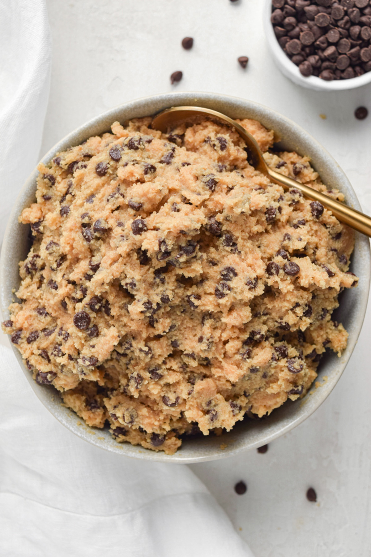 Overhead view of a bowl of keto cookie dough with a gold spoon on a white tabletop.