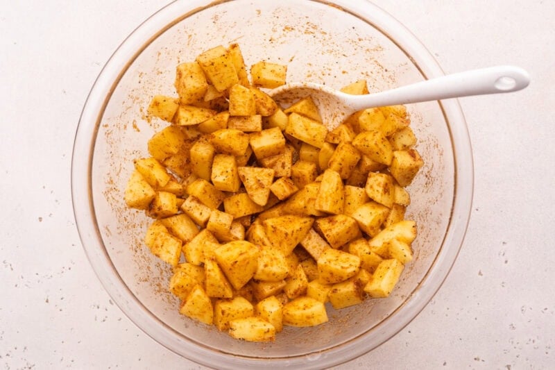 Overhead bowl with cubed potatoes, neutral oil, and several spices.