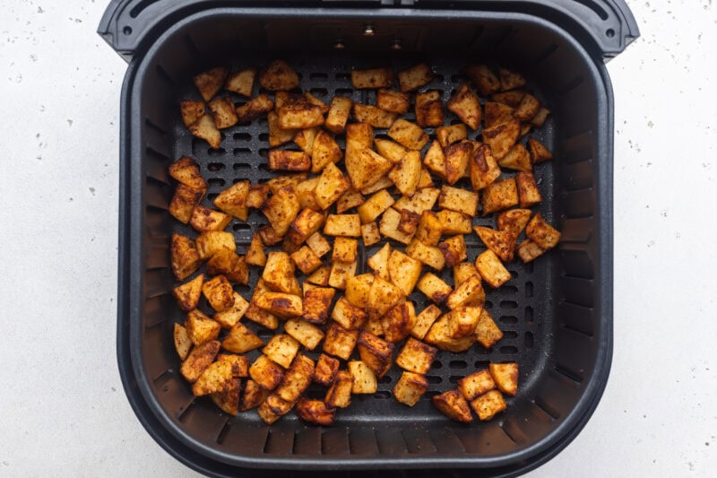 Overhead view of air fryer breakfast potatoes, fully cooked and golden brown, resting in an air fryer basket.