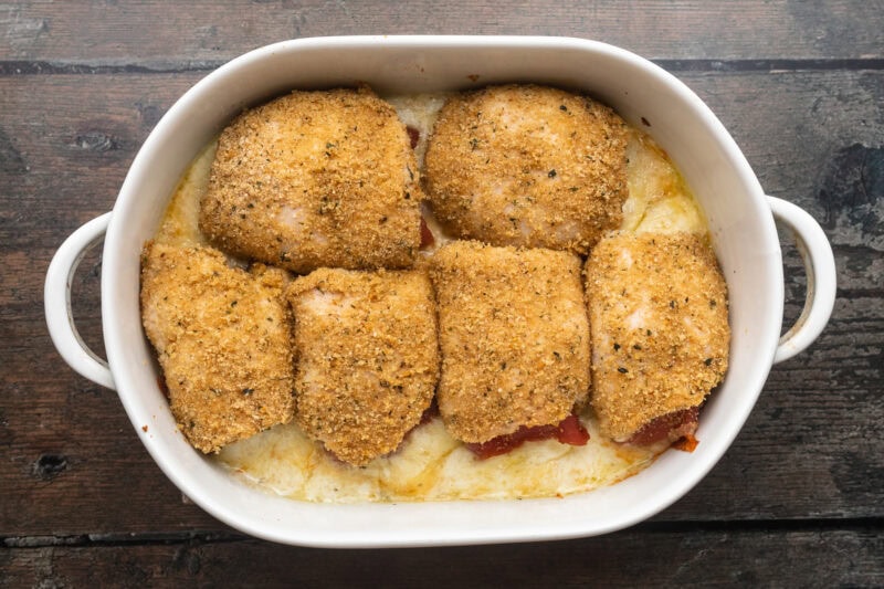 Baked chicken rollatini in a large white oval baking dish on a wooden table.