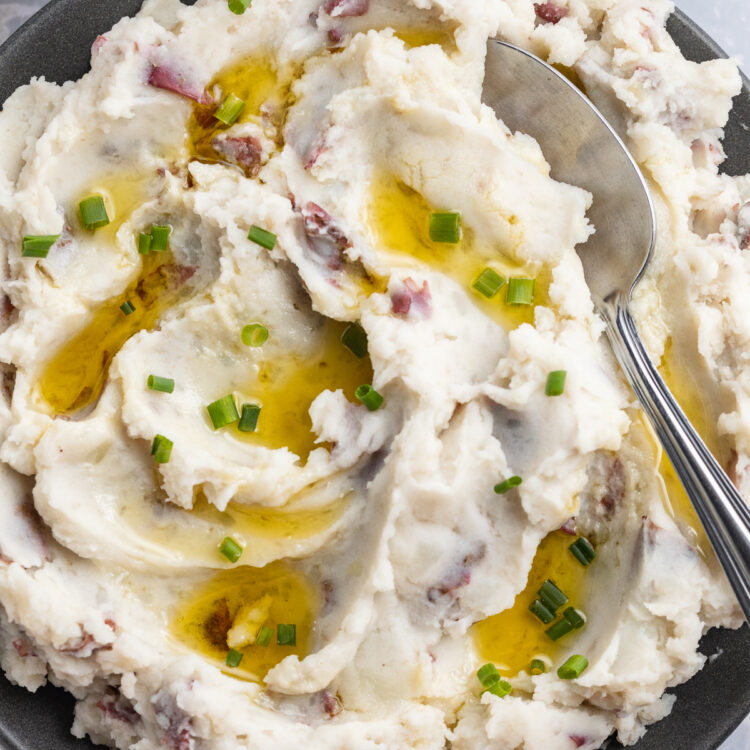 Fluffy, whipped, red skin mashed potatoes in a large blue-grey bowl with a spoon on a holiday table.