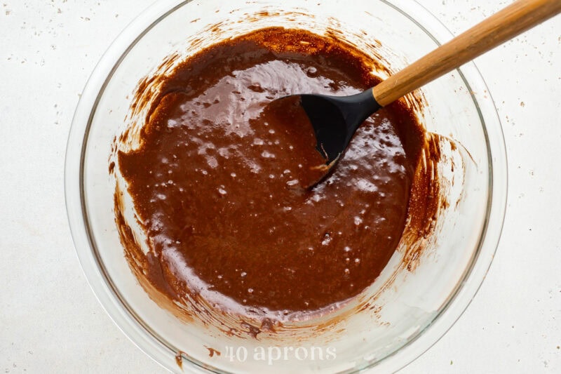 Brownie batter with chocolate chips folded in, sitting in a large glass mixing bowl with a silicone spatula.