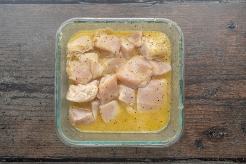 Chunks of chicken breasts marinating in a square glass pan filled with lemon juice and white wine.