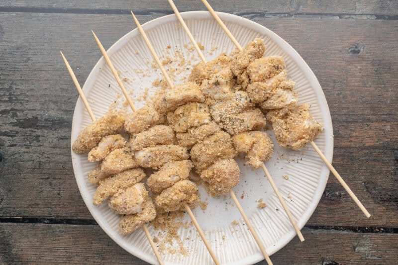 Skewered and breaded chicken chunks resting on a round white plate.