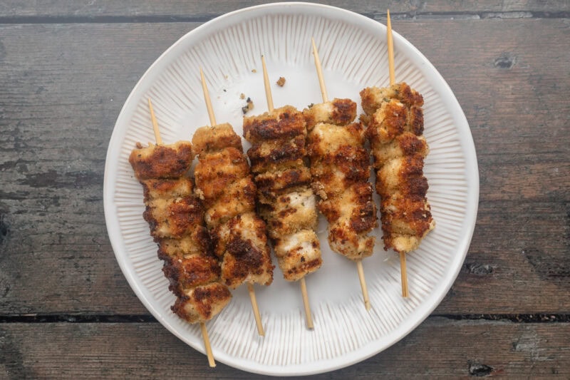 Grilled chicken spiedini skewers on a round white plate.