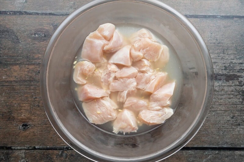 Overhead view of chicken chunks marinating in dill pickle juice in a large glass bowl.