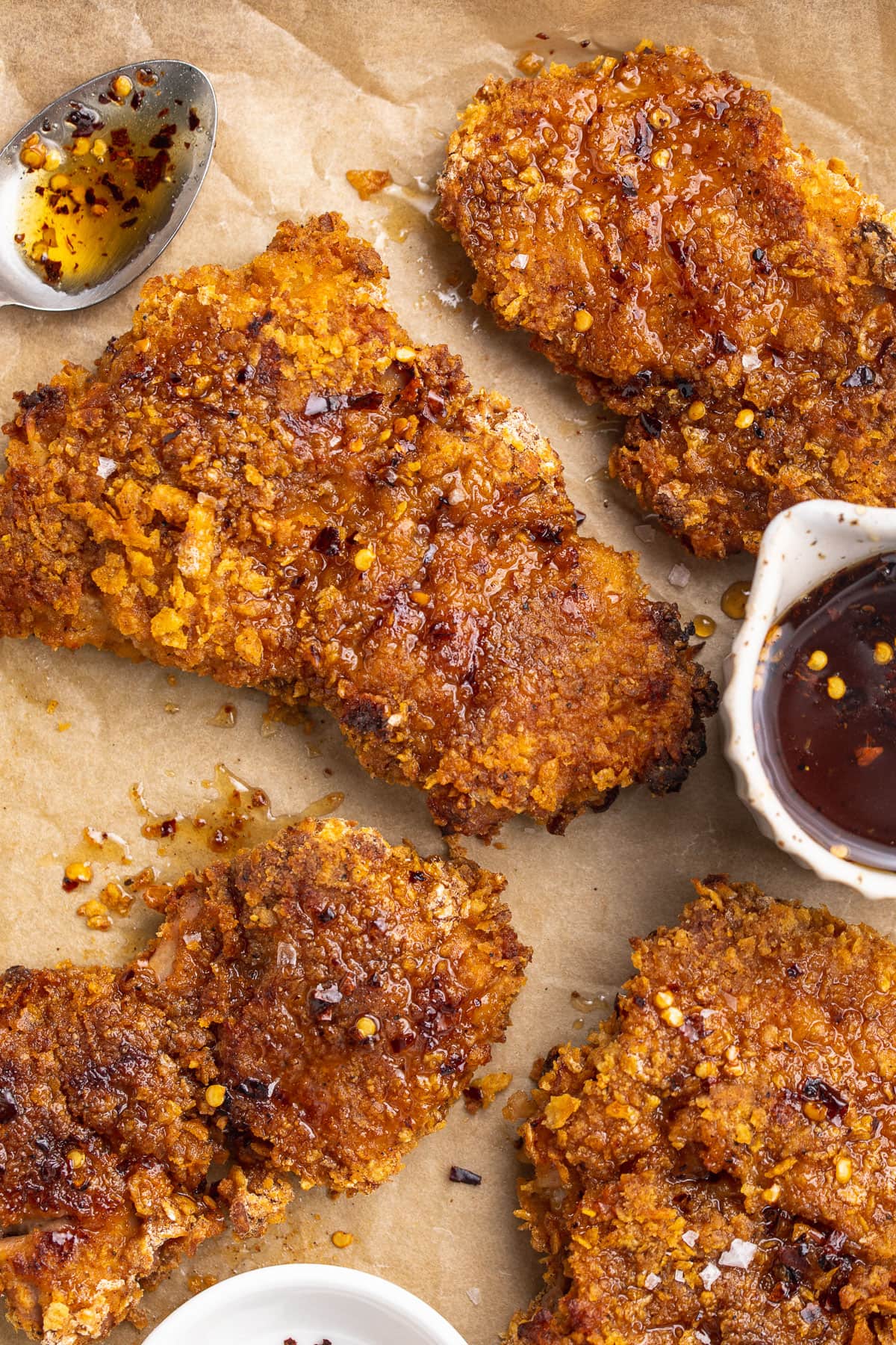 Hot honey chicken on a baking sheet lined with parchment paper next to a ramekin of hot honey sauce.