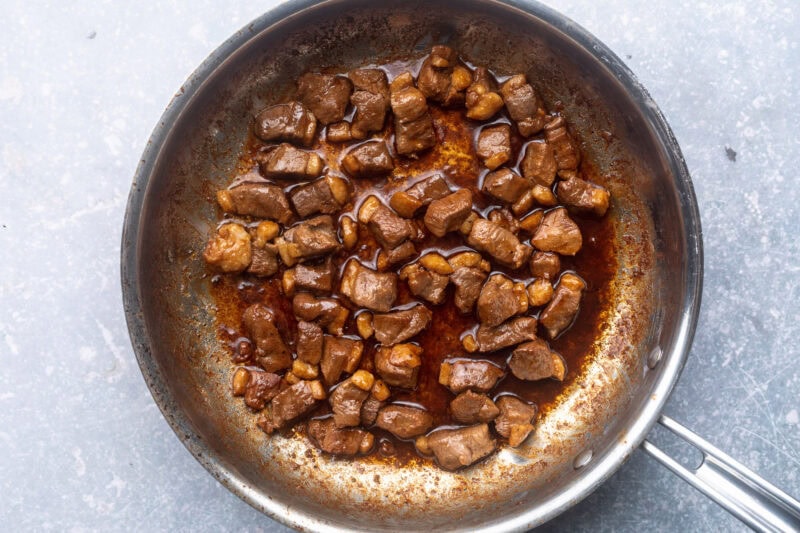 Seared bite-sized pieces of diced duck breast in a large silver skillet.