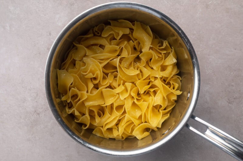 Al dente egg noodles in a large silver saucepan with a single silver handle.