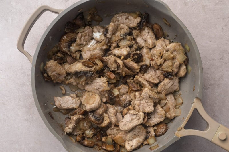 Strips of pork tenderloin in large skillet with sautéed mushrooms and diced onions.