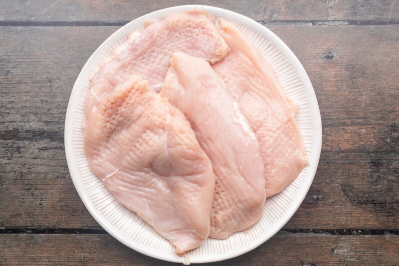 Raw chicken breasts on a round white plate.