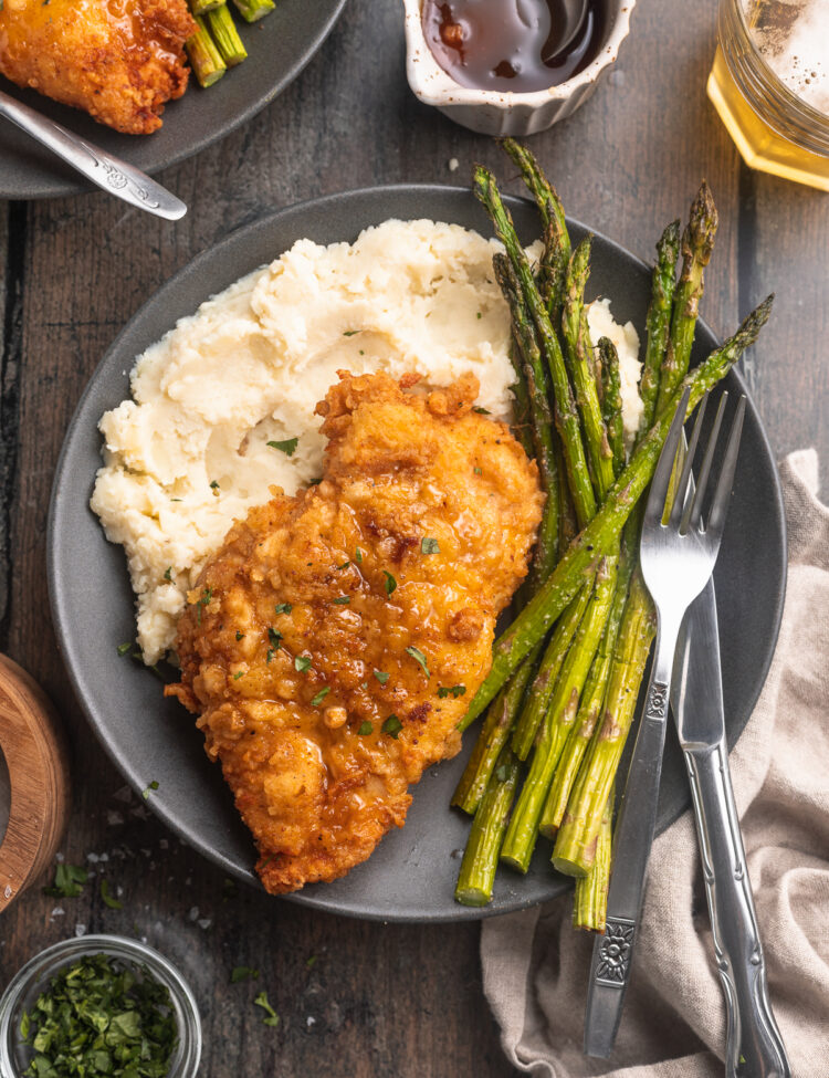 Truffle honey chicken plated with crisp, bright green asparagus and a bed of fluffy mashed potatoes.