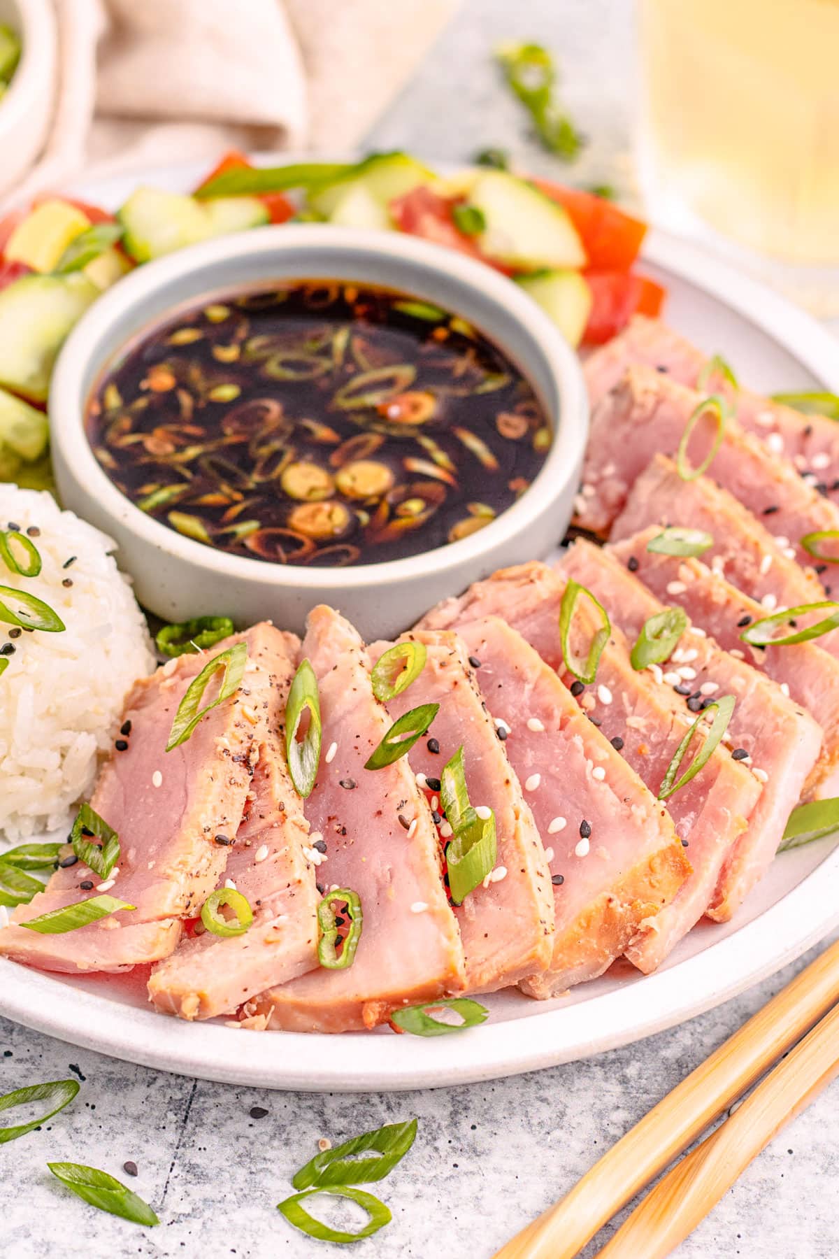 Air fryer tuna steaks, arranged in a semi-circle around a ramekin of soy sauce next to a mound of white rice garnished with sliced green onions.