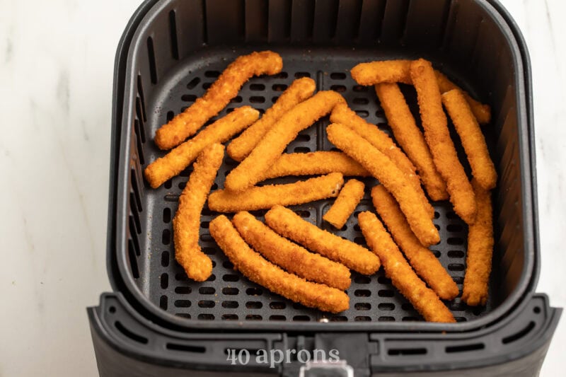 Frozen chicken fries in an air fryer basket.