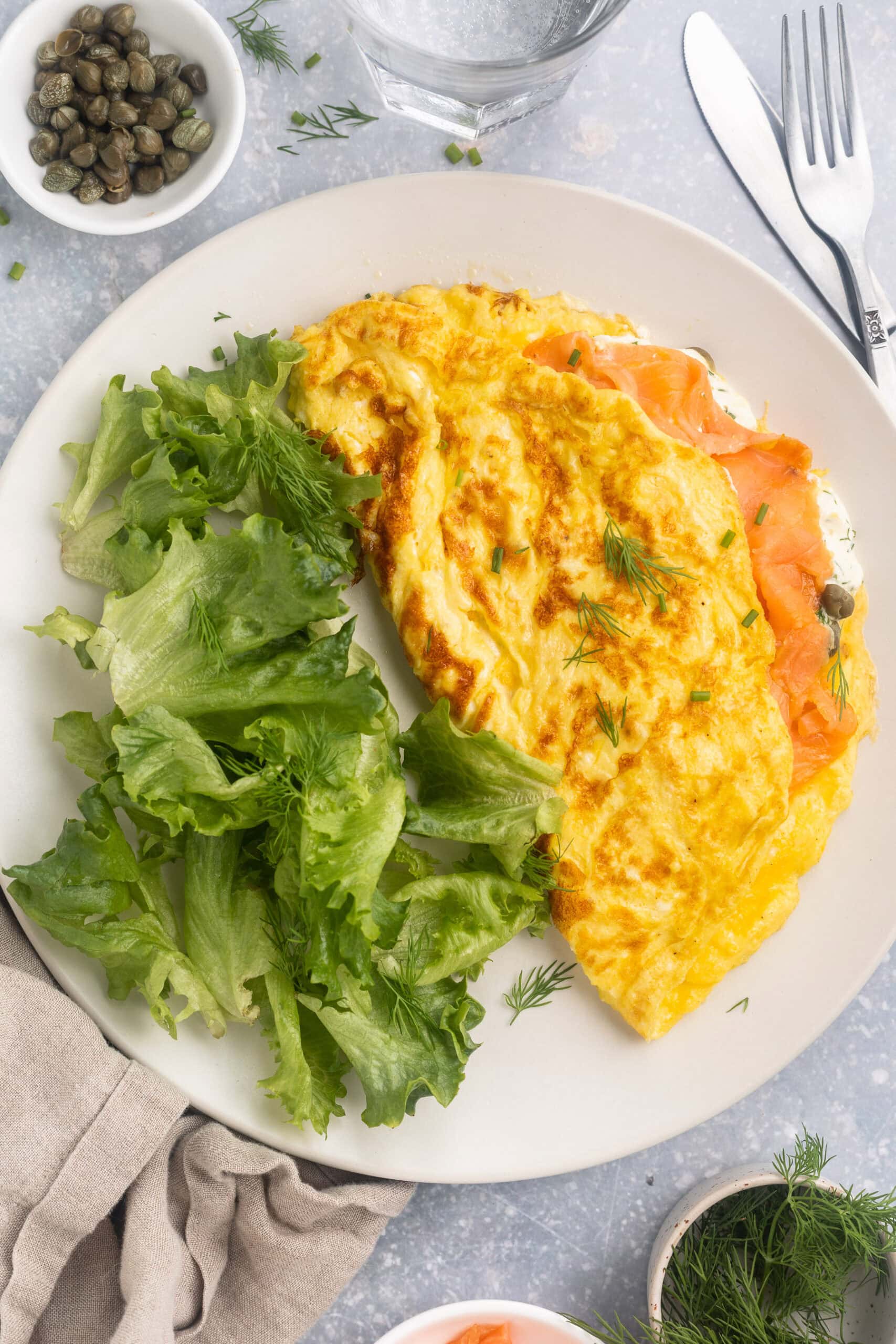 Overhead view of a folded salmon omelette on a plate with a green salad.