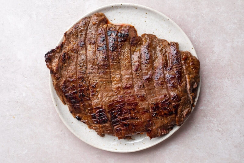 Seared flank steak on a white plate. Steak has been sliced into thick pieces.