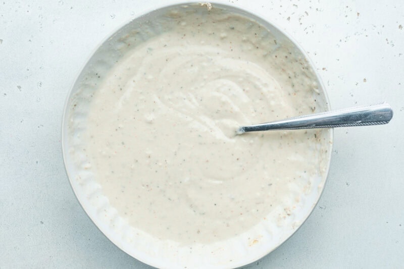 Batter mixture for vegan chicken fillet breading in a large white bowl with a spoon.