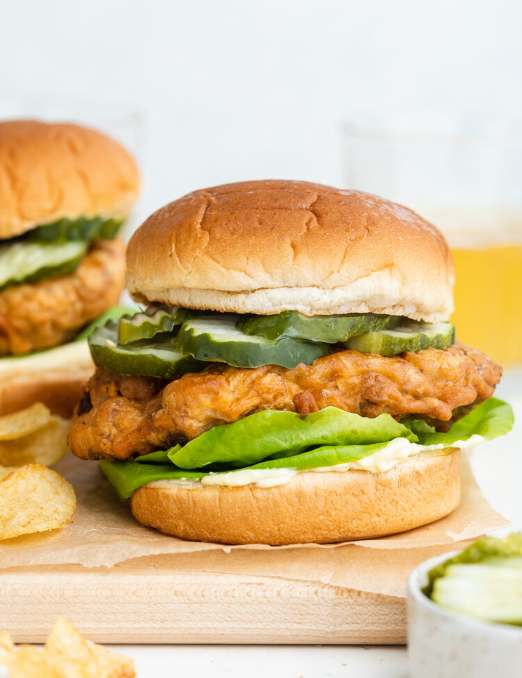 Side view of a fried vegan chicken sandwich with lettuce, mayo, and pickles on a serving tray.