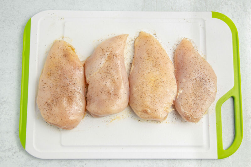 Seasoned chicken breasts on a cutting board.
