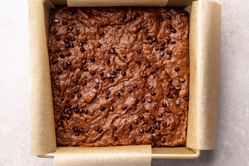 Top-down view of fully baked chocolate lactation brownies in a square baking pan with parchment paper hanging out the sides.