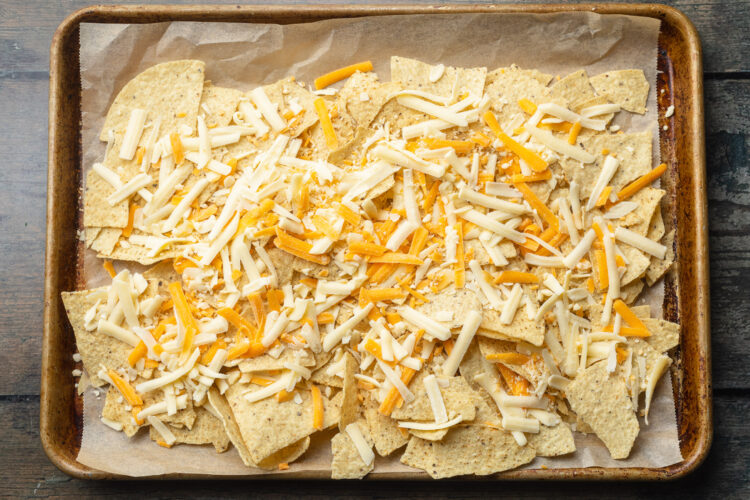 Tortilla chips topped with shredded cheese on a baking sheet.