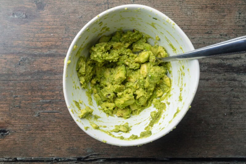 Mashed avocado with lime juice and salt in a mixing bowl with a fork.