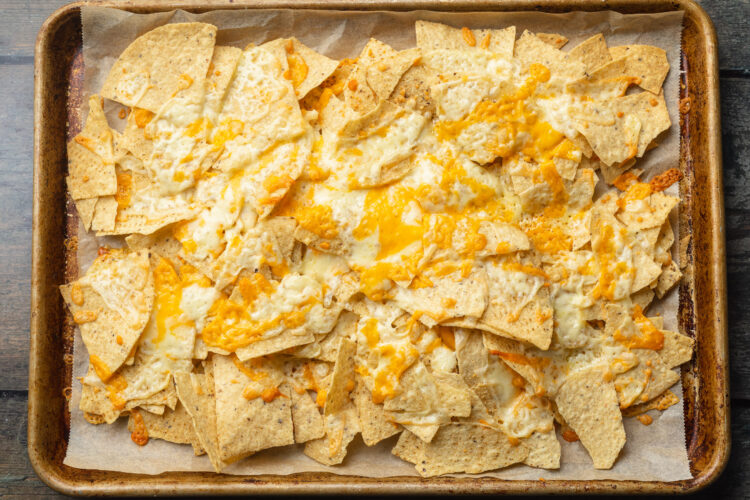 Melted shredded cheese on top of tortilla chips on a baking sheet.