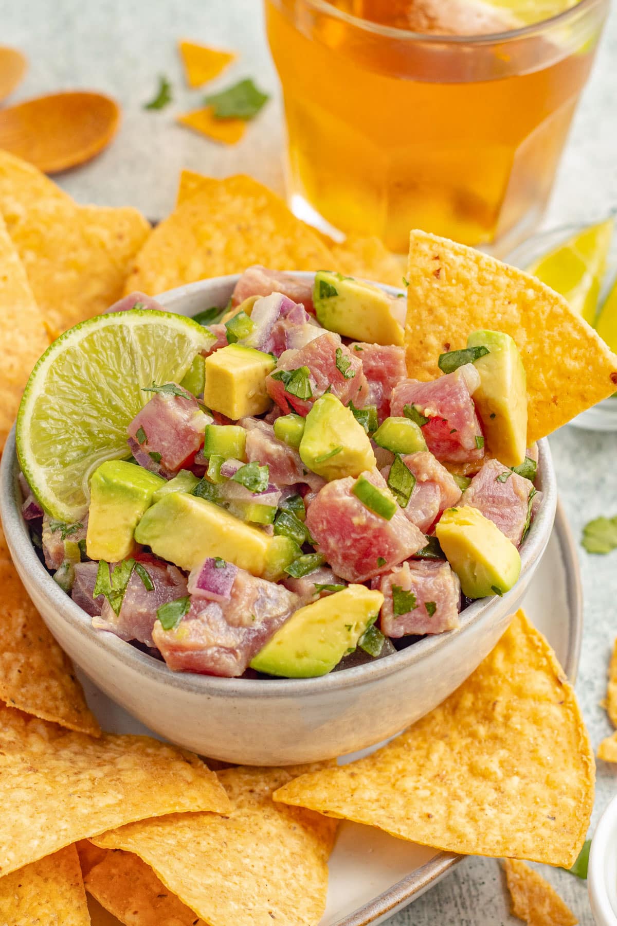 Side view of a bowl of tuna ceviche with chunks of ahi tuna, avocado, cilantro, and red onion with tortilla chips.