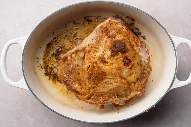 Seared and seasoned pork shoulder in large pot with oil.