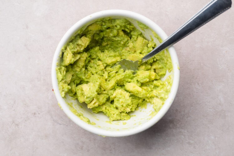 Guacamole in small white mixing bowl with a fork.