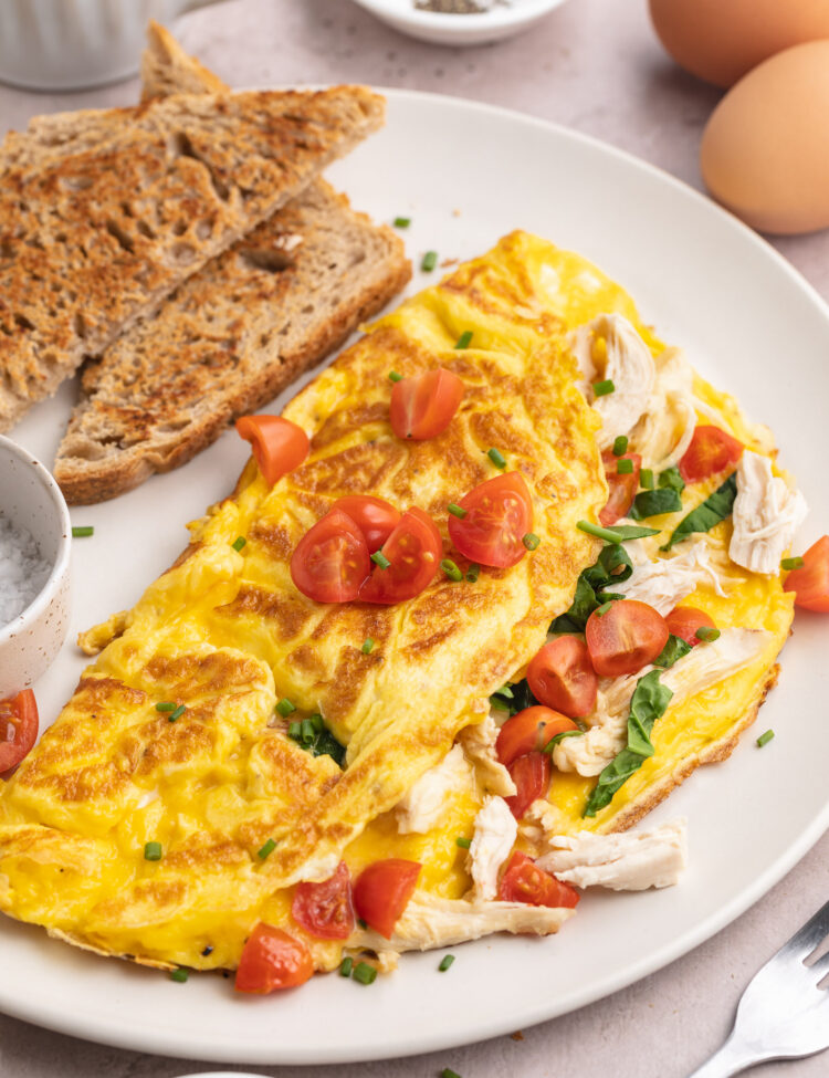 Angled view of a folded chicken omelette with tomatoes, cheese, spinach, and chicken.