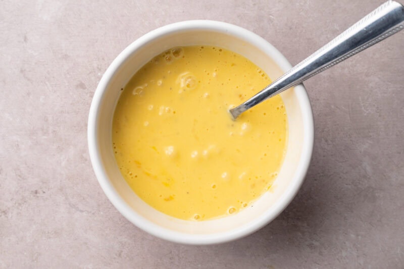 Eggs, milk, salt, and pepper in a small white mixing bowl with a silver fork.