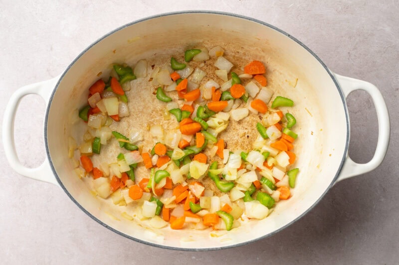 Top-down view of a large stock pot with oil, onions, carrots, and celery.