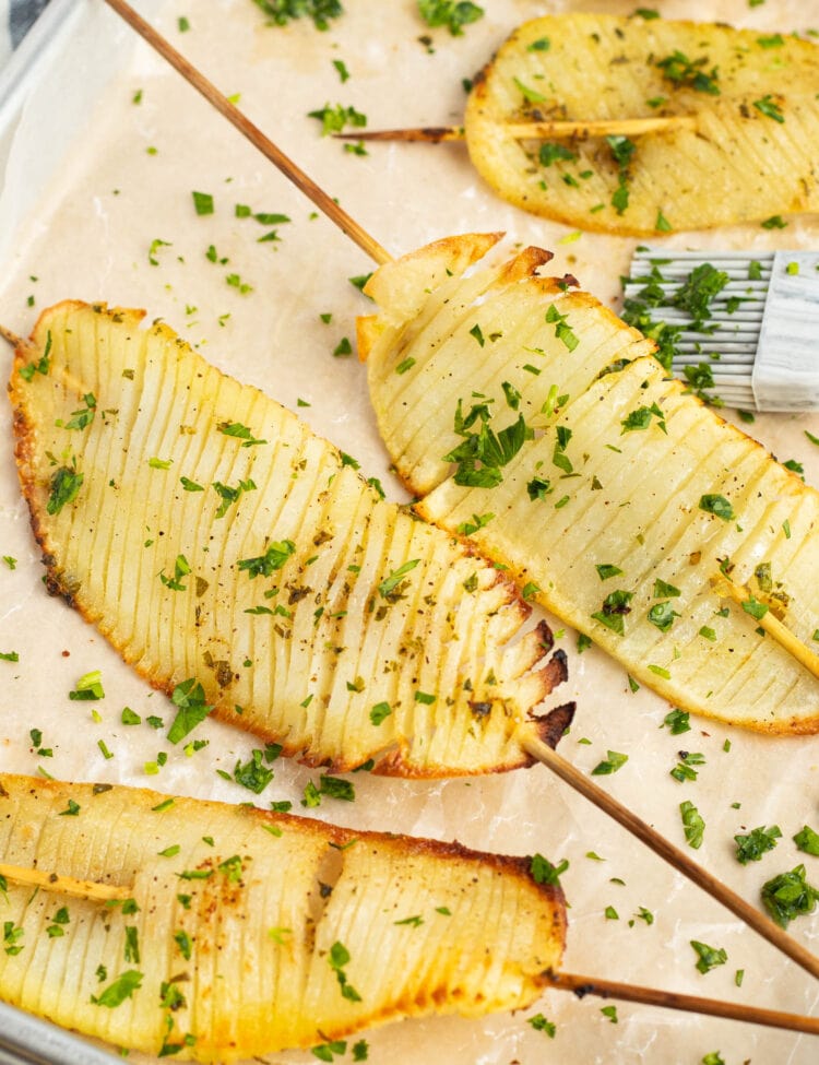 Accordion potatoes on skewers arranged on parchment paper.