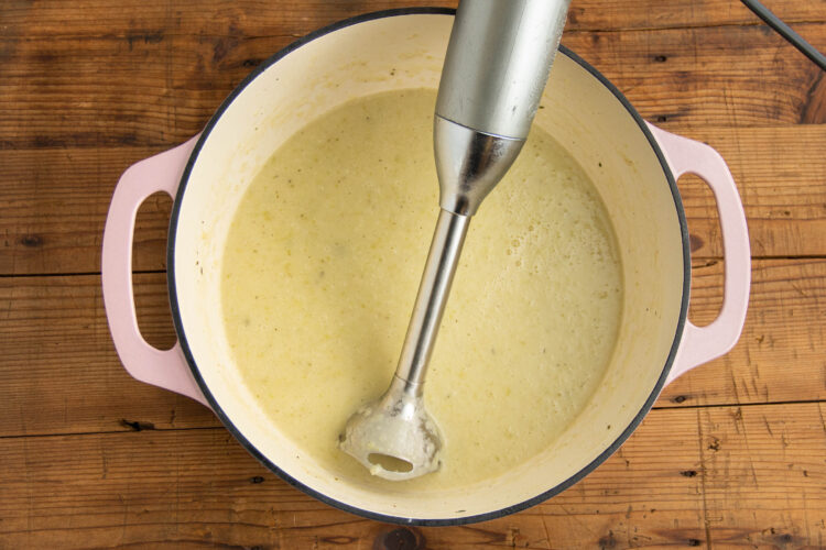 Immersion blender in large pot with smooth cream of onion soup.