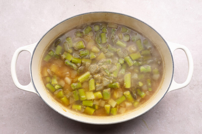 Asparagus, broth, and other ingredients for potato asparagus soup in a large dutch oven.